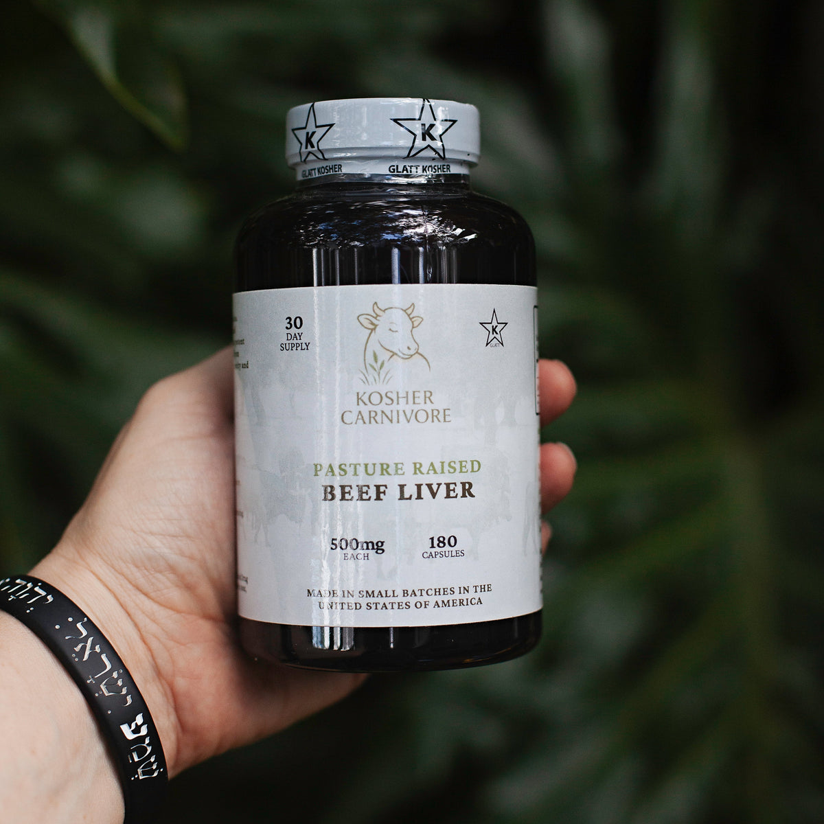 Hand holding a supplement bottle labeled 'Kosher Carnivore' against a dark background